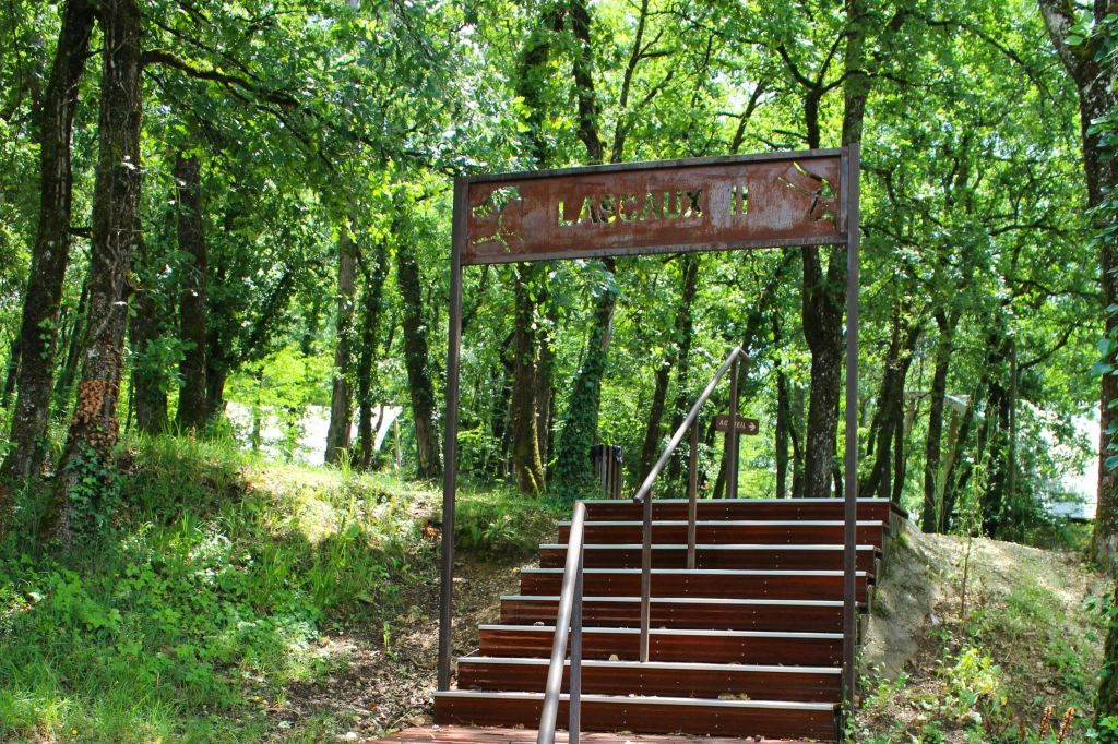 울창한 푸른 나무와 초목으로 둘러싸인 꼭대기에 'Lascaux II' 라고 적힌 표지판이 있는 숲 속 계단.