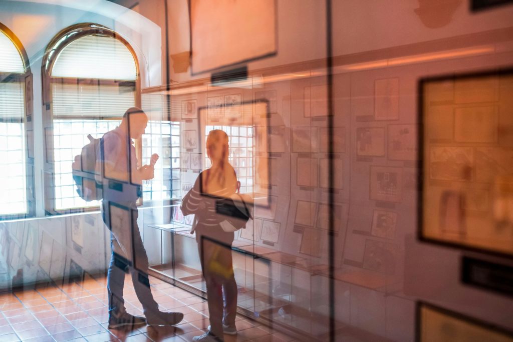 따뜻한 조명으로 액자에 담긴 작품을 전시하는 유리 패널에 비친 갤러리 분위기의 두 사람.