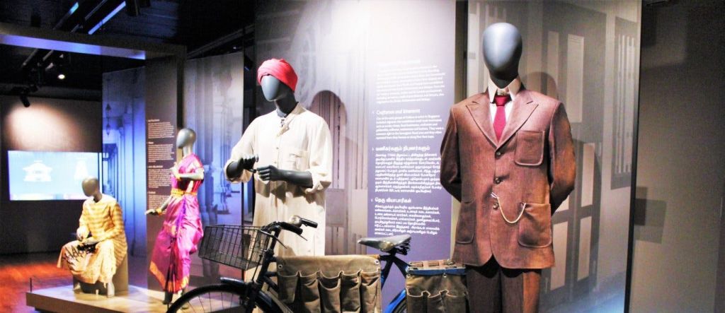 박물관 진열대에 패니어가 놓인 자전거 옆에서 전통적이고 격식 있는 복장을 한 마네킹.