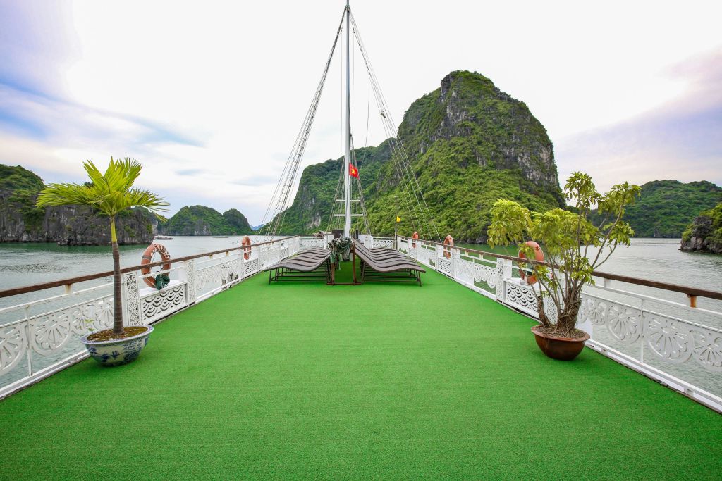 녹색 바닥, 빈 라운지 의자, 화분이 있는 선박 데크는 녹색의 바위섬을 배경으로 하고 있습니다.