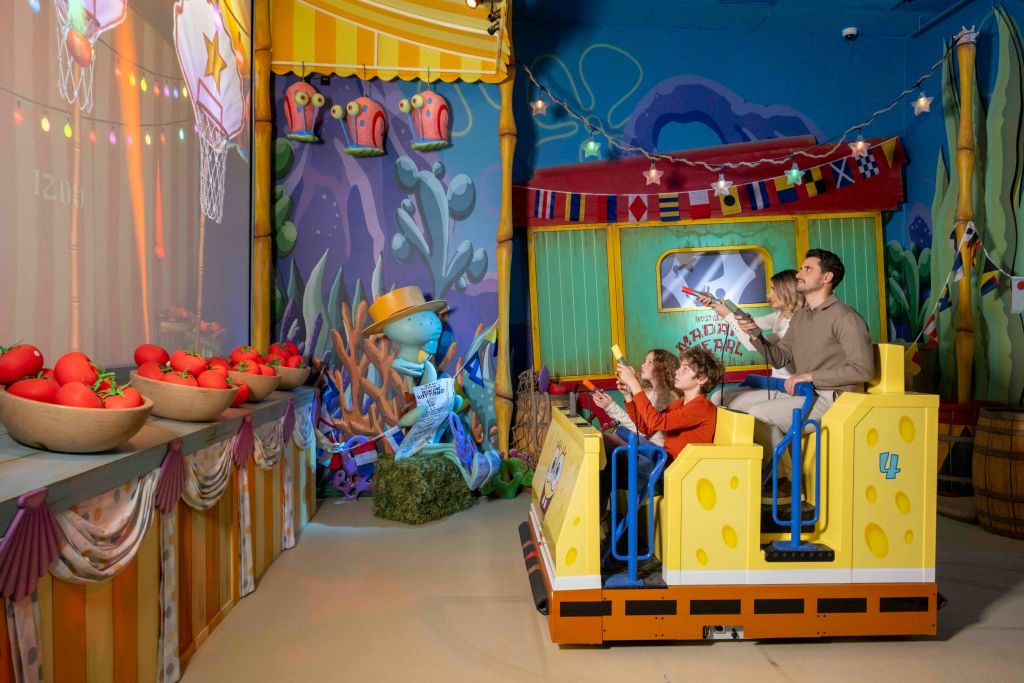 수중 테마 놀이공원에서 장난감 총을 조준하는 테마 차량에 탑승한 두 사람.