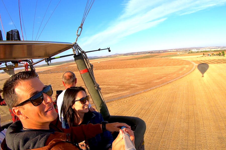 활짝 핀 들판과 맑고 푸른 하늘을 배경으로 열기구에 탄 세 사람이 셀카를 찍고 있습니다.