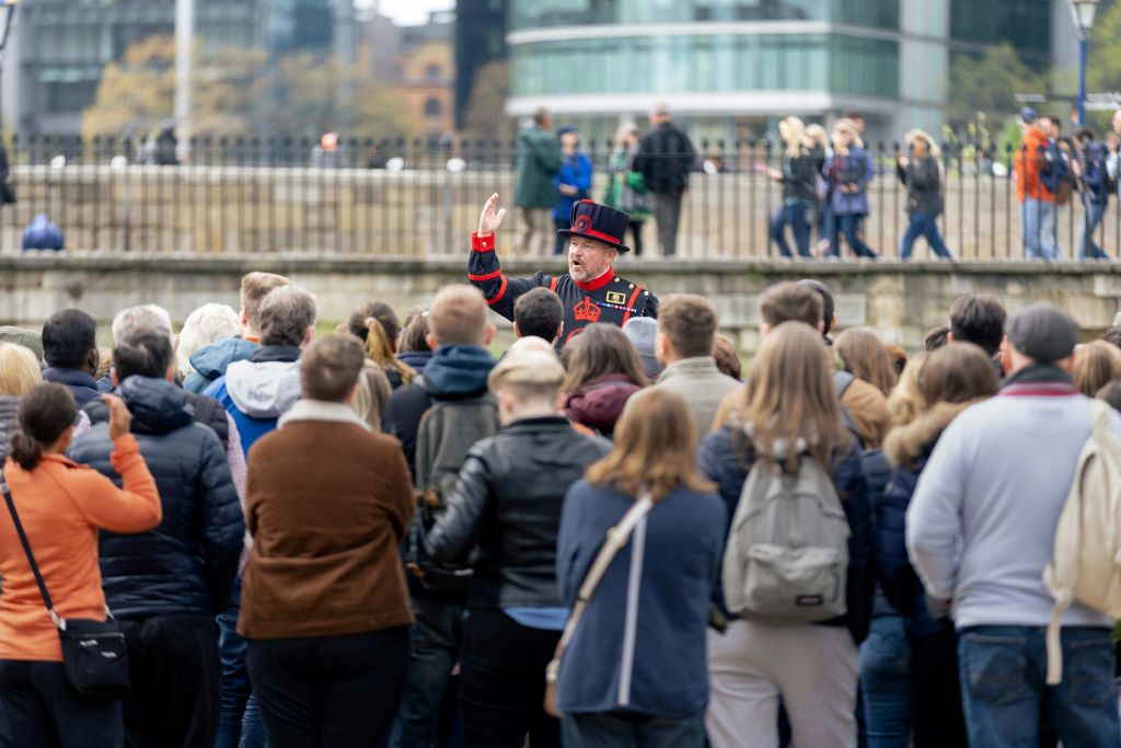 전통 복장을 한 투어 가이드가 현대적인 건물을 배경으로 야외에서 수많은 사람들을 만나고 있습니다.