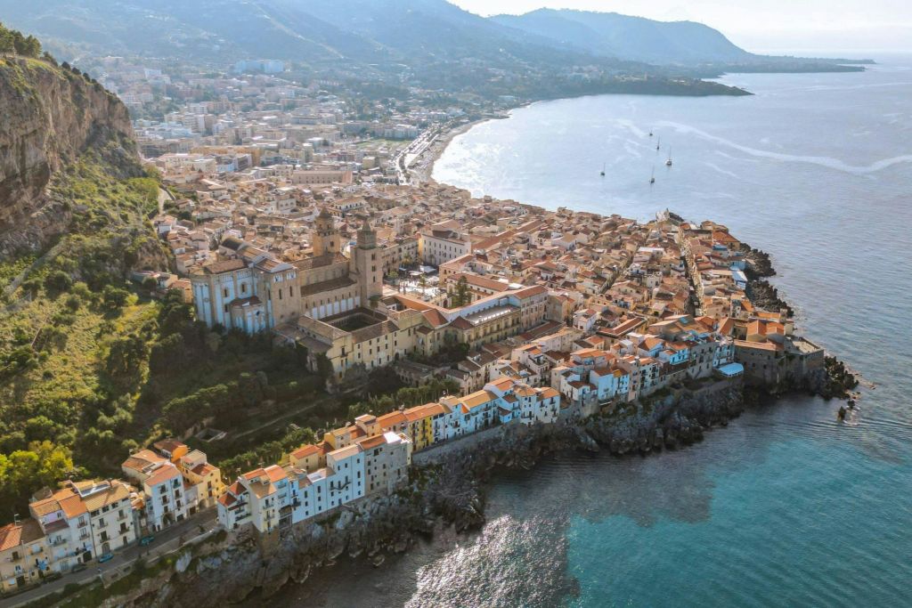 빽빽한 건물, 눈에 띄는 대성당, 바다로 이어지는 험준한 절벽이 있는 해안 마을의 공중 전망.