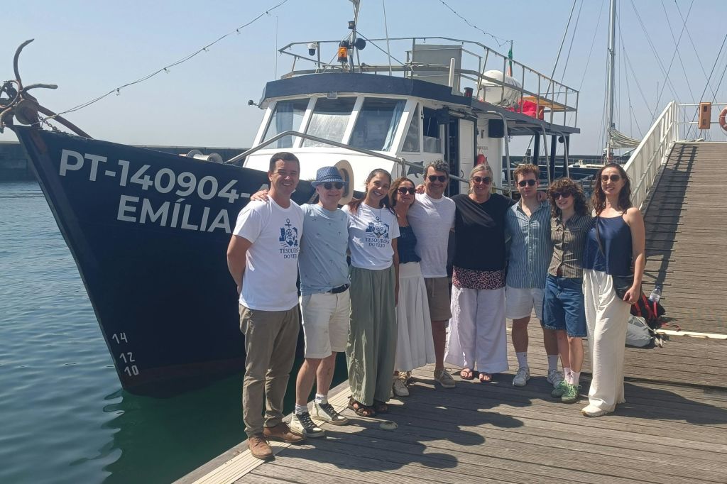 8명으로 구성된 그룹이 보트 앞 선착장에 서서 화창한 날 사진을 찍기 위해 미소를 짓고 포즈를 취하고 있습니다.