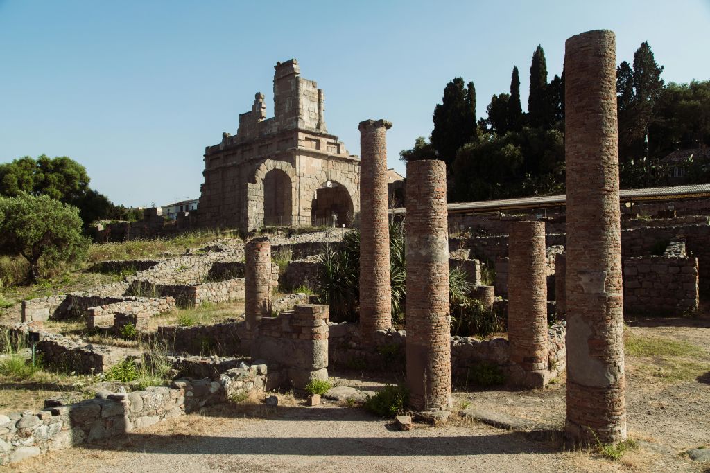 석조 기둥과 아치가 있는 고대 유적은 맑은 하늘을 배경으로 녹지와 먼 나무로 둘러싸여 있습니다.