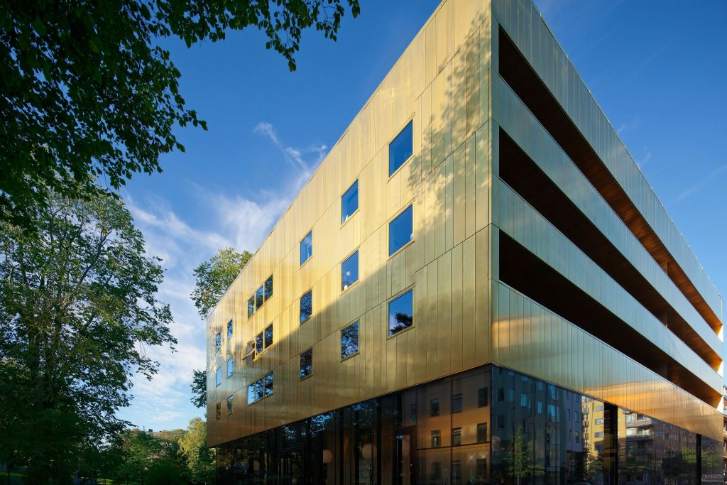 황금색 상단 부분과 수많은 창문이 있는 현대적인 건물로, 맑고 푸른 하늘에 나무가 둘러싸여 있습니다.