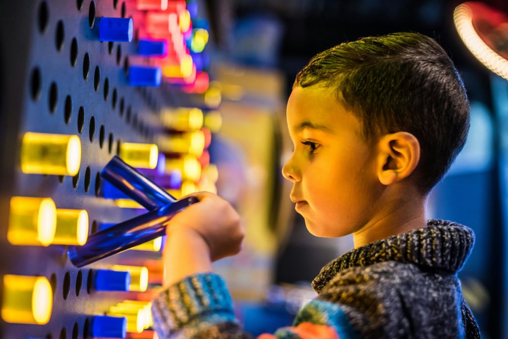 줄무늬 스웨터를 입은 어린 아이는 화려한 조명과 버튼에 집중하여 아케이드 게임을 할 수 있습니다.