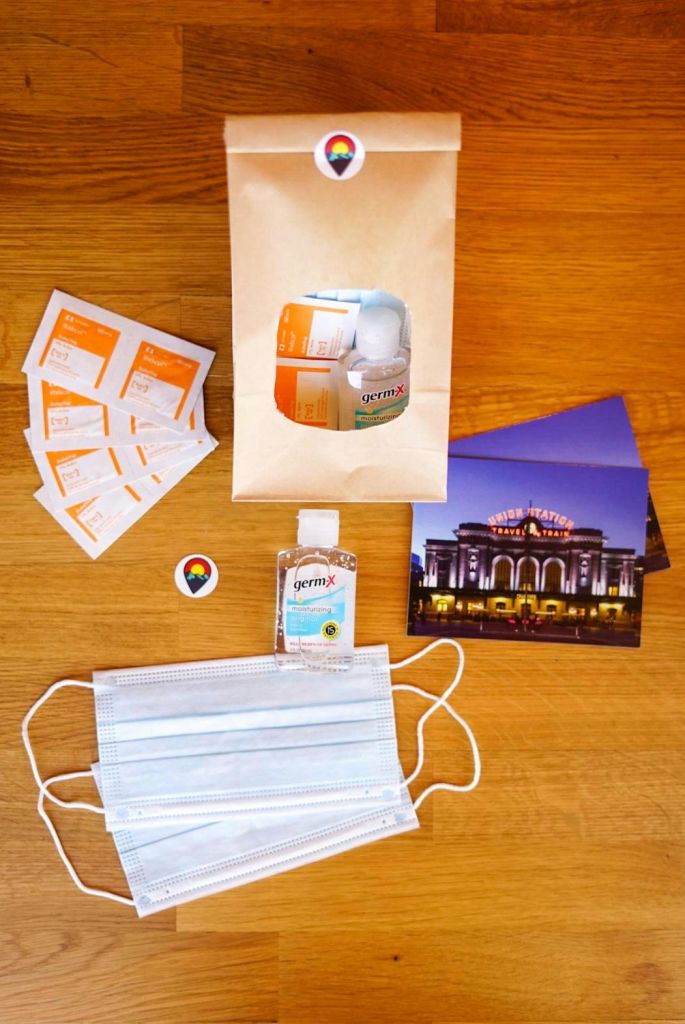 마스크, 손 소독제, 소독용 물티슈, 엽서, 나무 표면에 놓인 종이 봉투 등 평평한 물품이 놓여 있습니다.