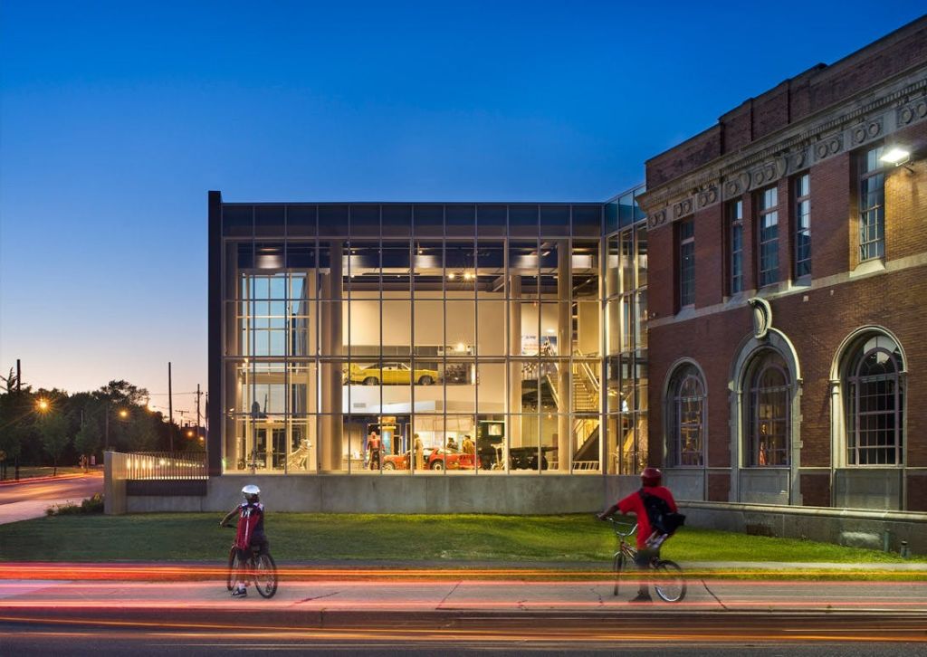 해질 무렵 벽돌 구조물 옆의 밝고 현대적인 유리 건물 옆으로 두 명의 자전거 운전자가 지나갑니다.