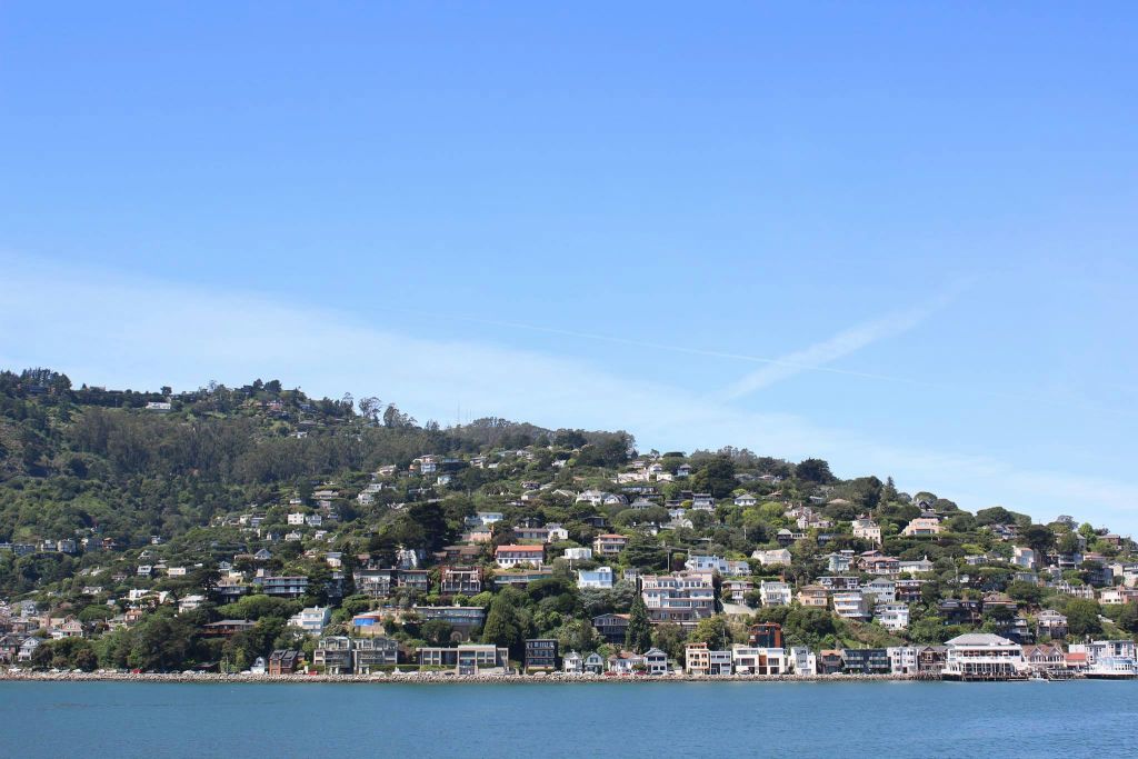 맑고 푸른 하늘 아래 물가에 건물들이 줄지어 있는 주택과 녹지로 뒤덮인 언덕.