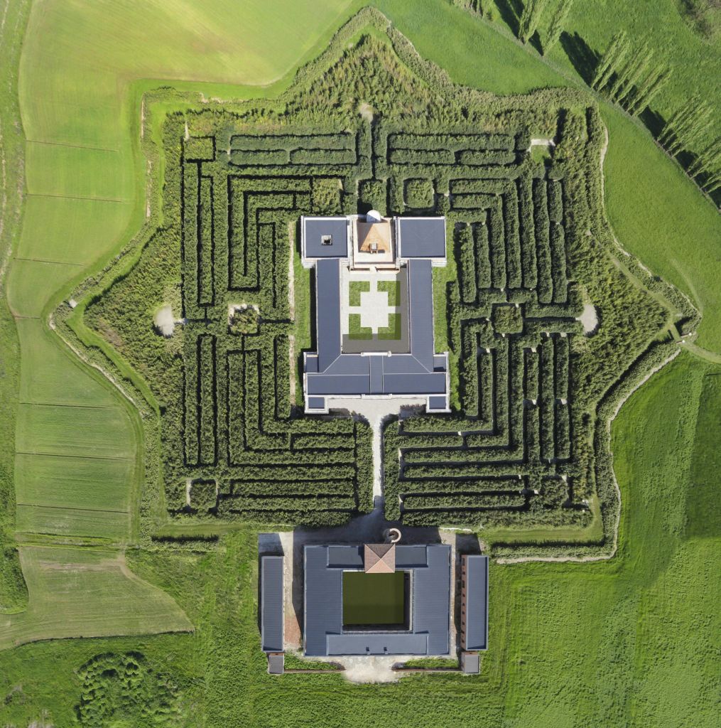 녹음이 우거진 중앙 건물을 둘러싸고 있는 기하학적 울타리 미로의 공중 전망. 경로는 미로 안에서 볼 수 있습니다.