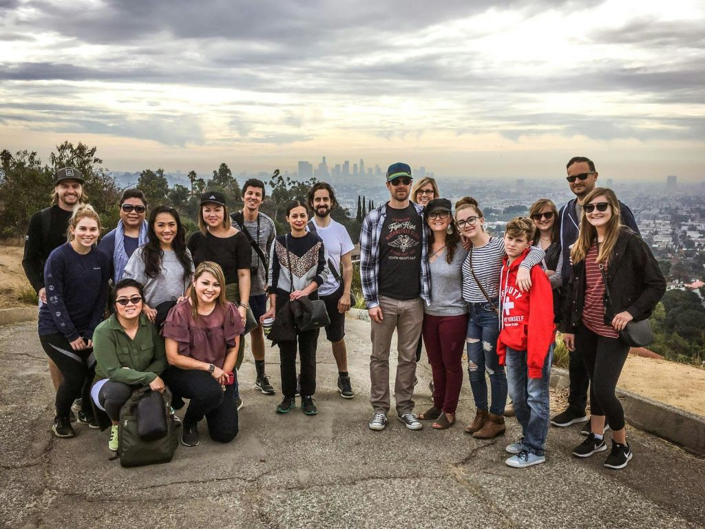 한 무리의 사람들이 먼 도시 풍경과 흐린 하늘을 배경으로 야외 포즈를 취하고 있습니다.