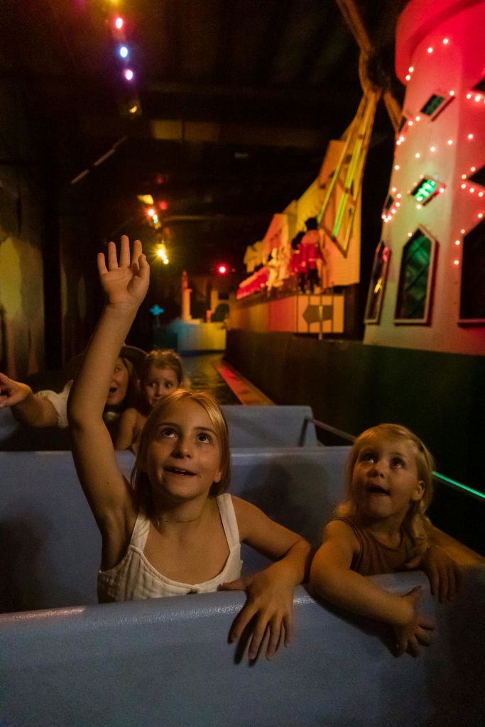 어두운 놀이 기구를 타고 있는 어린이들. 한 소녀는 손을 들고 다른 소녀들은 앞의 애니메이션 장면을 흥미진진하게 바라봅니다.
