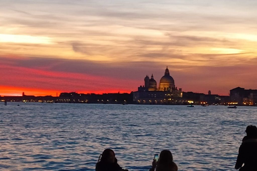 도시 스카이라인의 실루엣과 돔형 건물을 배경으로 해질녘 바닷가 근처의 두 사람.