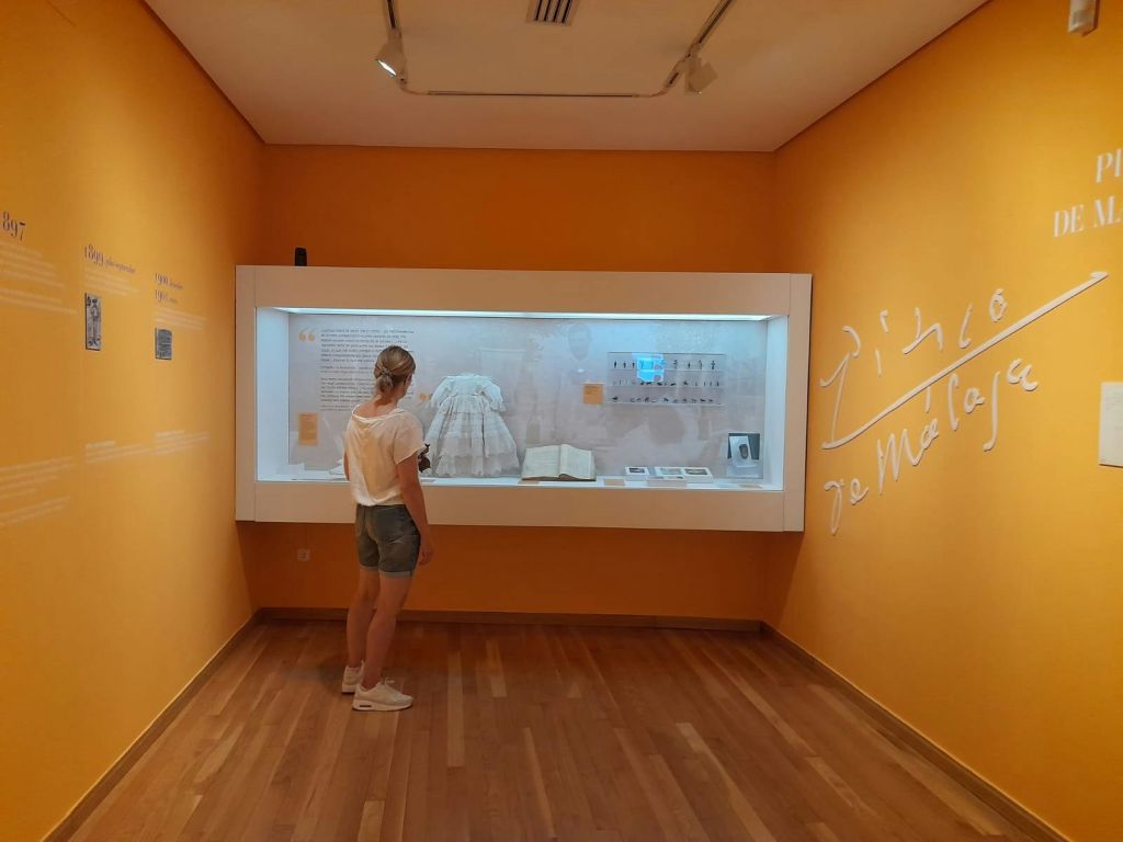 한 사람이 주황색 벽이 있는 작은 방에서 역사적 유물이 전시된 박물관 진열장 앞에 서 있습니다.