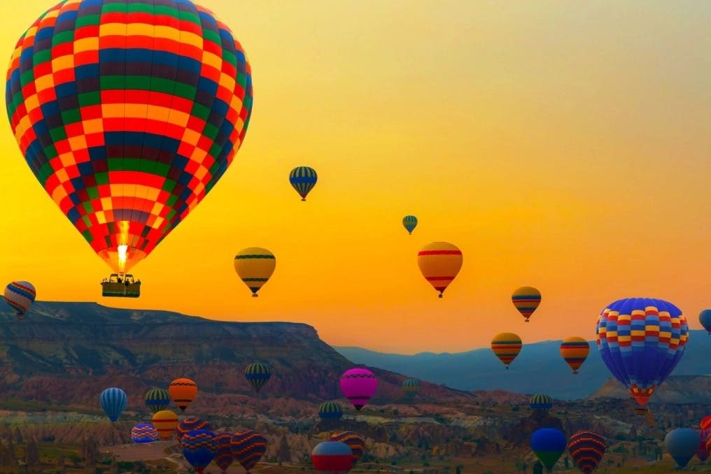해가 질 무렵 험준한 풍경 위로 수많은 다채로운 열기구가 떠 있습니다.