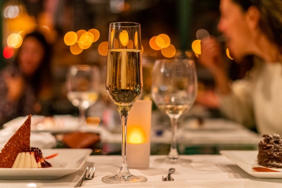 레스토랑 분위기에서 샴페인 한 잔, 접시에 담긴 디저트, 흐릿한 따뜻한 조명을 클로즈업으로 감상해보세요.