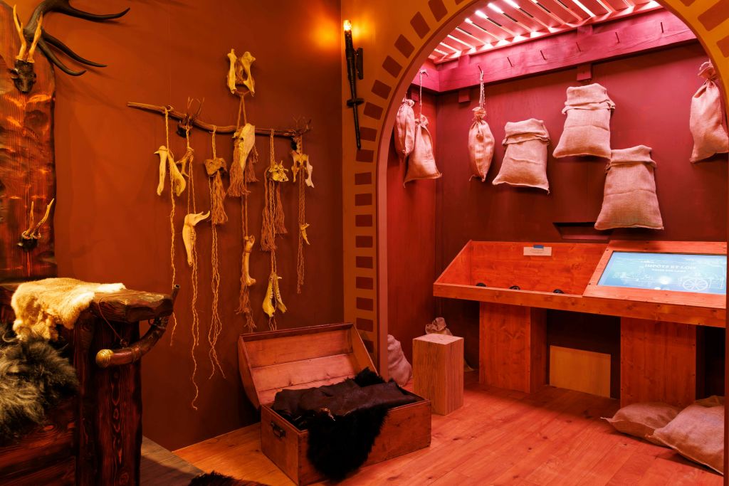 나무 상자가 있고, 말린 식물이 걸려 있으며, 삼베 자루가 있는 방. 따뜻한 조명과 소박한 인테리어가 아늑한 분위기를 연출합니다.