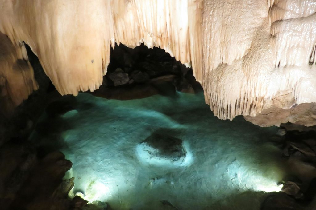 청록색의 맑은 물과 물에 잠긴 바위가 있는 조명이 희미한 동굴 수영장 위에는 종유석이 매달려 있습니다.