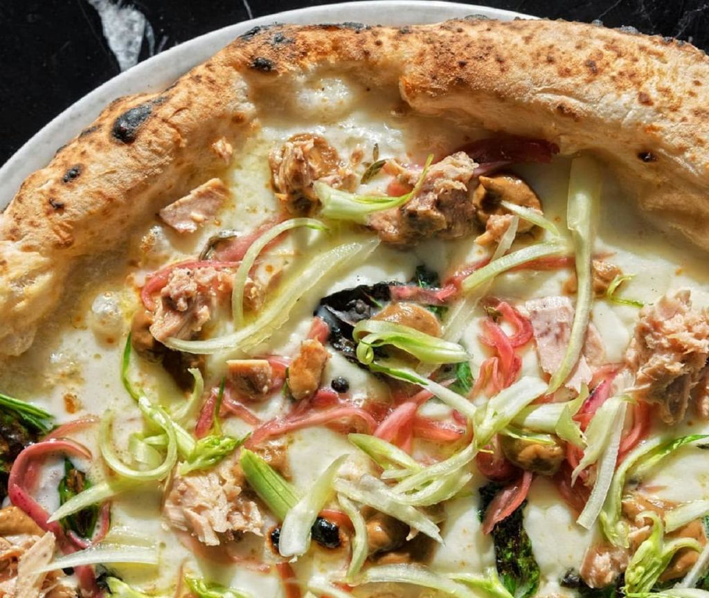 얇게 썬 크러스트에 치킨, 얇게 썬 파, 분홍색 양파를 토핑한 피자를 클로즈업한 사진입니다.