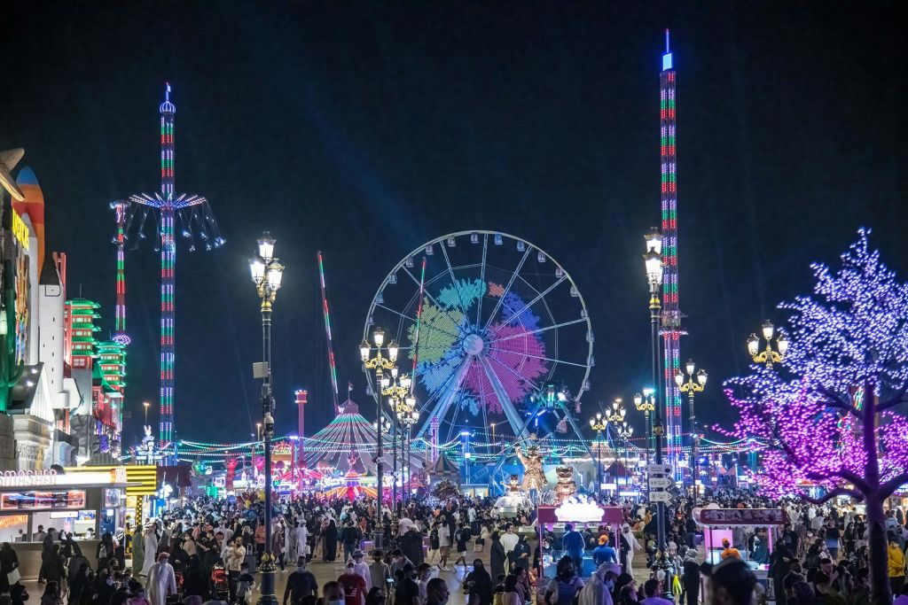 대관람차, 높은 놀이기구, 화려한 조명, 수많은 사람들이 축제를 즐기는 북적이는 야간 카니발입니다.
