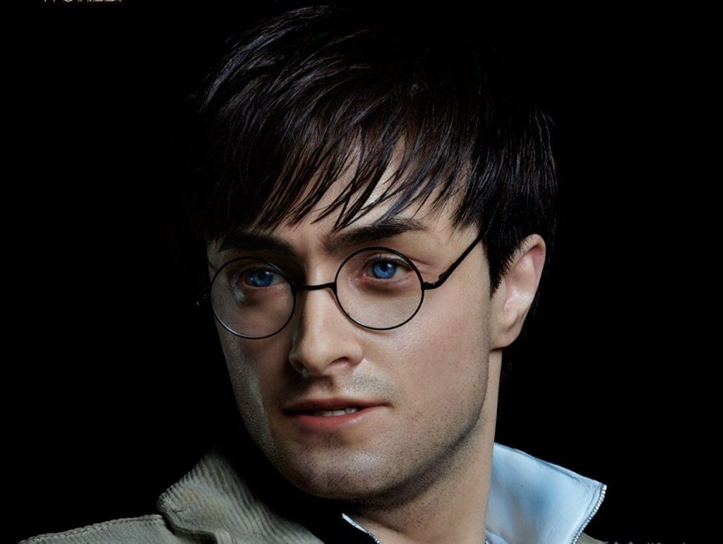 둥근 안경과 밝은 색상의 셔츠를 입은 짧은 검은 머리의 사람이 검은색 배경을 배경으로 포즈를 취하고 있습니다.