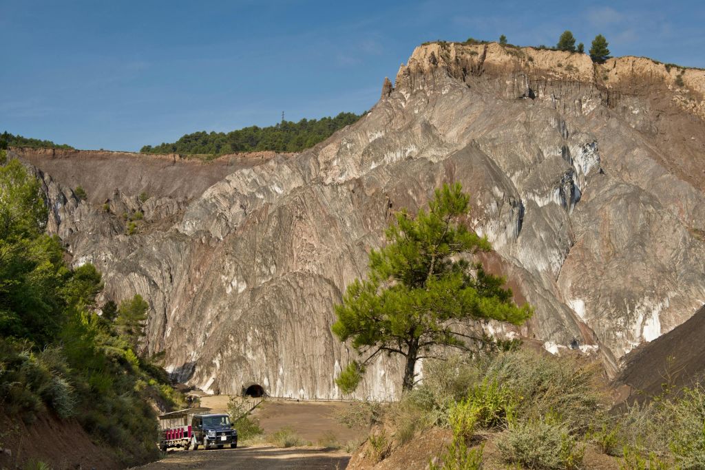 커다란 바위산, 터널 입구, 푸른 나무, 맑고 푸른 하늘 아래 주차된 차량이 있는 험준한 풍경.