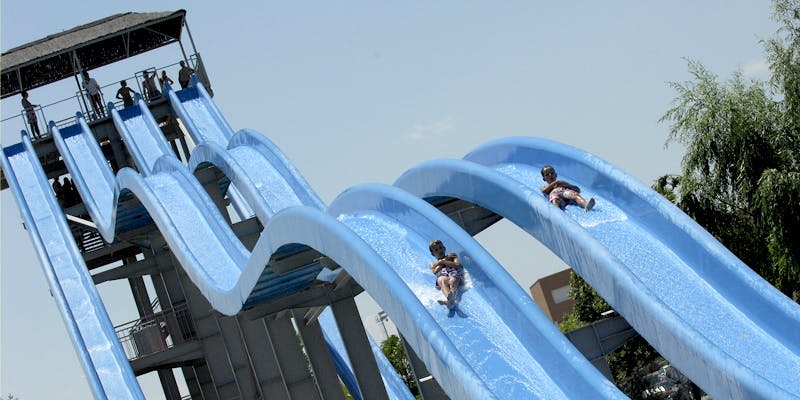 화창한 날 평행한 푸른 물 미끄럼틀을 따라 미끄러져 내려가는 두 아이.