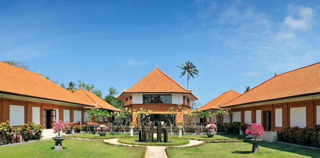 주변의 작은 구조물, 울창한 녹음, 맑고 푸른 하늘을 배경으로 한 커다란 주황색 지붕 건물입니다.