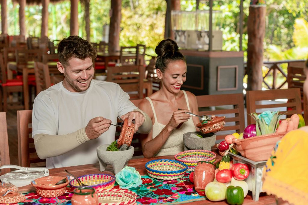 한 남녀가 소박한 레스토랑의 화려한 테이블에 앉아 짠 바구니로 둘러싸인 그릇과 식기가 담긴 음식을 준비하고 있습니다.