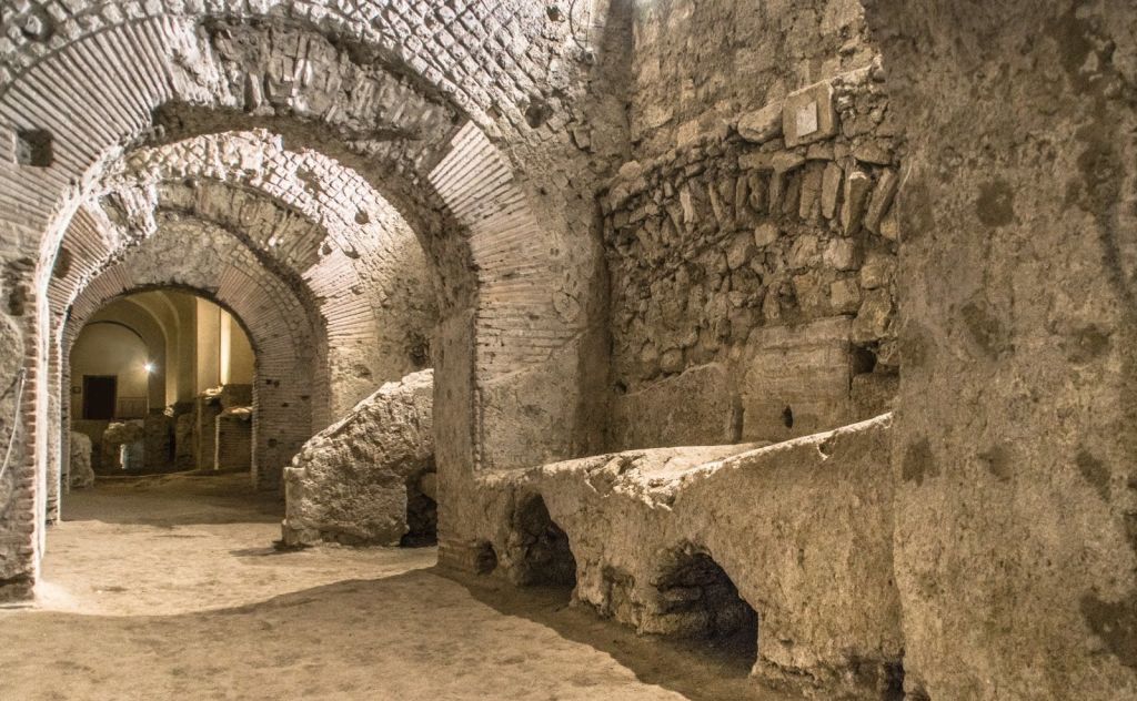 고대 석조와 벽돌로 된 아치형 통로와 조명이 희미한 벽, 지하 유적지 또는 거친 표면과 아치형 천장이 있는 역사적인 장소.