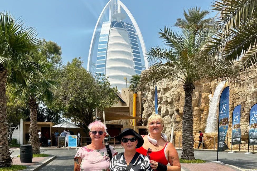 야자수와 화창한 하늘로 둘러싸인 버즈 알 아랍 호텔 앞에서 세 사람이 야외 포즈를 취하고 있습니다.