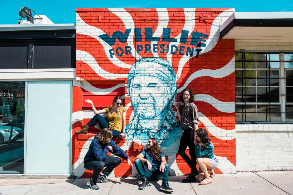 한 무리의 사람들이 초상화가 그려진 화려한 벽화 앞에서 "대통령을 위한 윌리" 라는 글씨로 포즈를 취하고 있습니다.