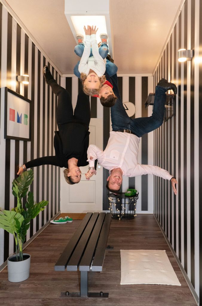 검은색과 흰색 줄무늬 벽이 있는 방에 4명이 거꾸로 매달려 있어 착시 효과를 연출합니다.