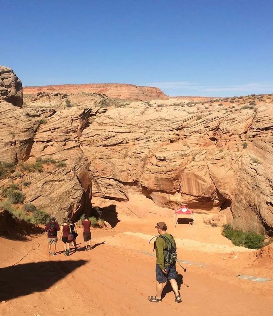 저 멀리 작은 빨간 텐트가 있는 맑고 푸른 하늘 아래 바위 협곡을 향해 걸어가는 등산객들.