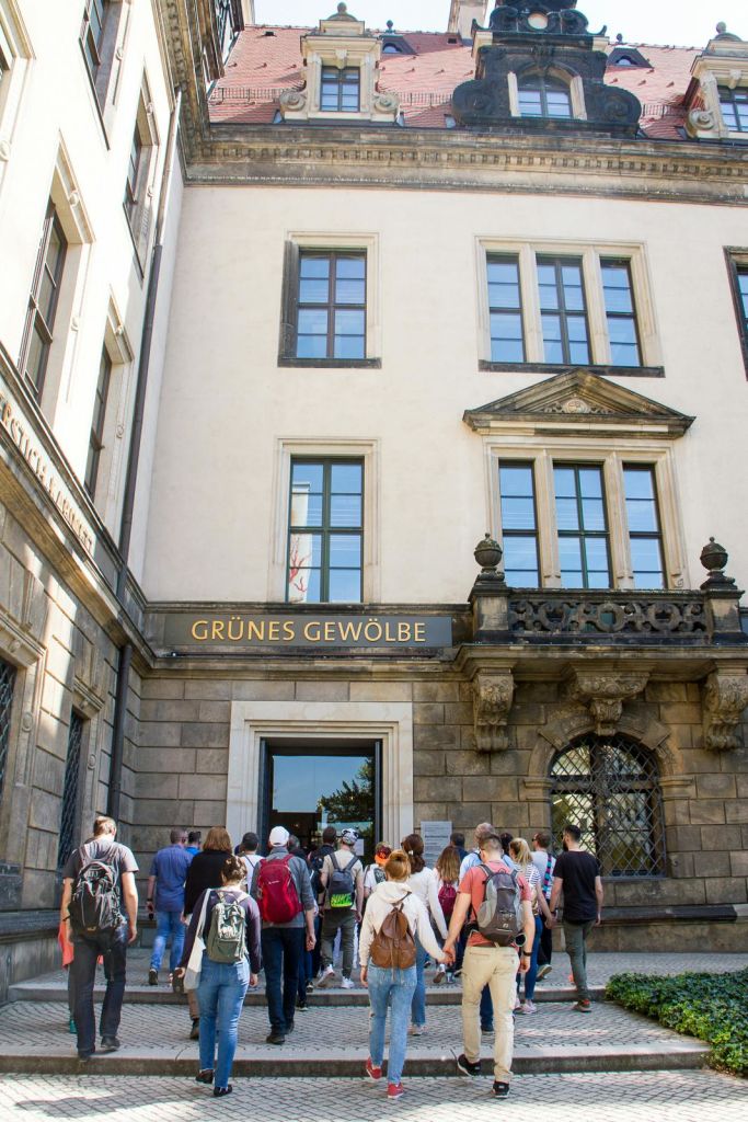 커다란 창문과 유서 깊은 건축물이 있는 입구 위에 'GRUNES GEWÖLBE' 표지판이 있는 건물에 들어서는 사람들.