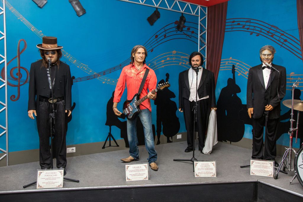 각각 마이크를 든 실물 크기의 뮤지션 왁스 형상 세 개가 파란색 배경과 악보가 있는 무대에 서 있습니다.