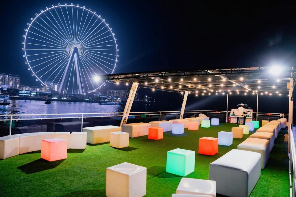 옥상 테라스의 다채로운 큐브 좌석, 현악기 조명, 커다란 관람차를 배경으로 펼쳐지는 야경.