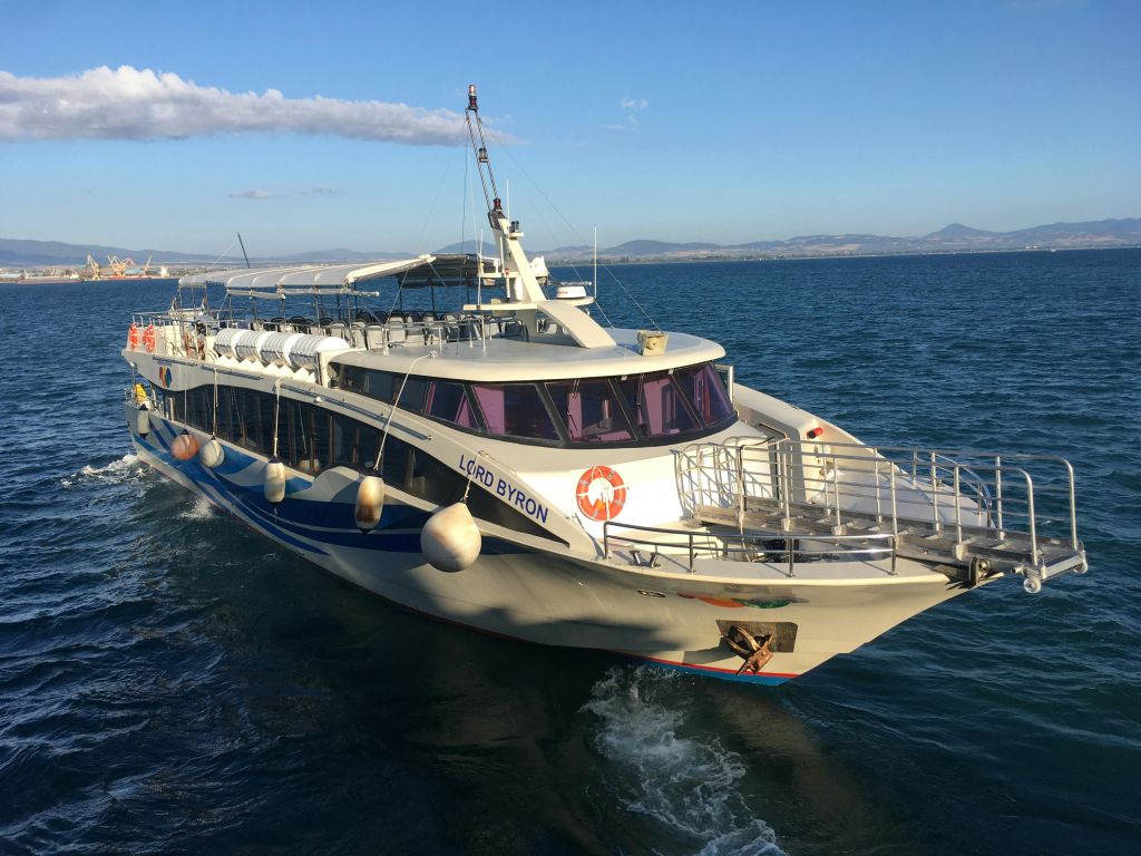 "바이런 경" 이라는 이름의 흰색 여객선이 맑은 하늘 아래 잔잔한 푸른 바다를 항해합니다. 산이 배경으로 보입니다.