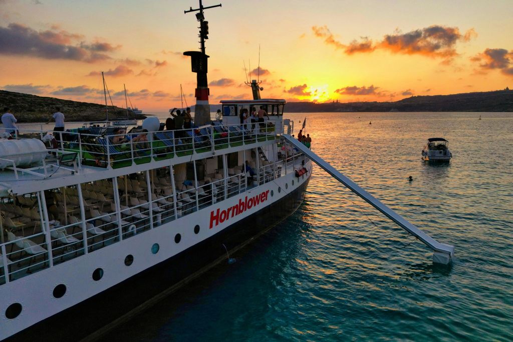 해질녘 고요한 바다에서 즐기는 '혼블로어' 라는 이름의 보트. 갑판에 사람들이 보이고 아름다운 해안선이 배경으로 펼쳐집니다.