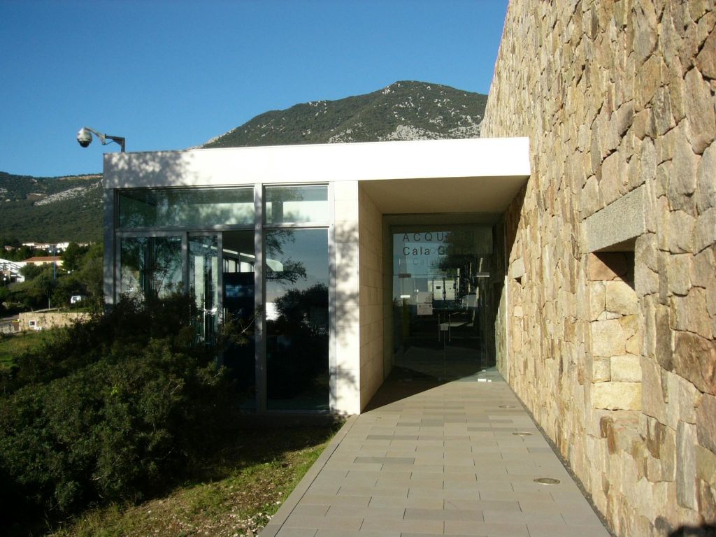 유리 벽, 석조 외관, 유리 출입문으로 이어지는 포장된 통로가 있는 현대적인 건물입니다. 산을 배경으로.