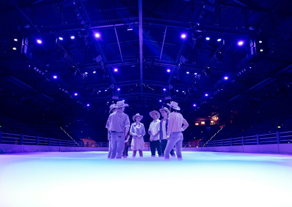 카우보이 모자를 쓴 사람들이 보라색 조명 아래 밝고 안개로 뒤덮인 아이스링크에 서 있습니다.