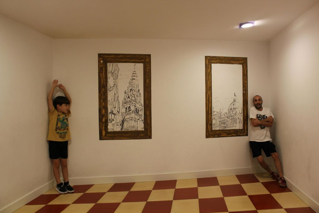 스포츠웨어를 입은 한 남성이 빨간색과 베이지색 체크무늬 바닥에 서 있는 건축 스케치 액자가 있는 흰색 벽에 기대어 있습니다.