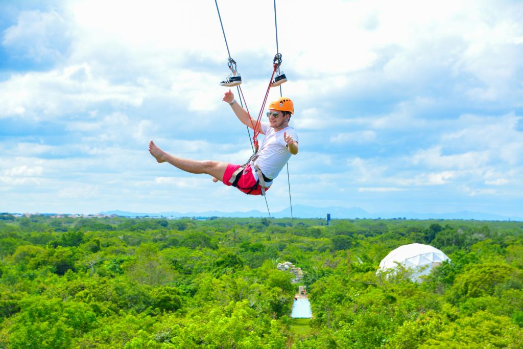 흐린 하늘을 배경으로 헬멧과 선글라스를 착용한 사람이 울창한 푸른 숲 위에 지퍼 라이닝을 하고 있습니다.