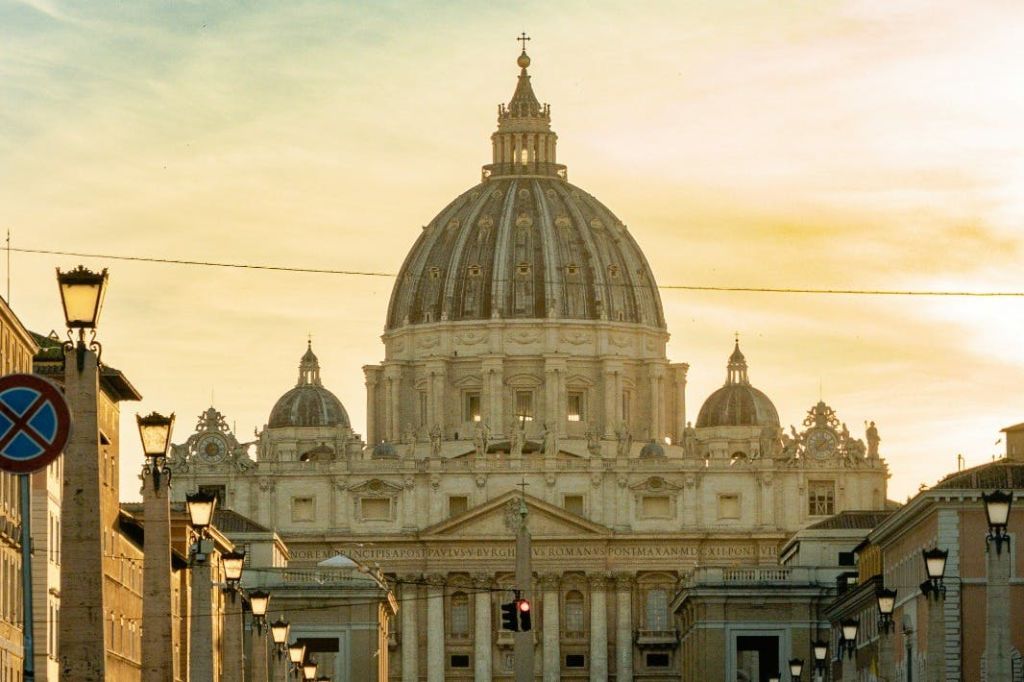 화려한 건축물이 있는 커다란 돔형 건물, 작은 돔으로 둘러싸인 건물, 노을이 질 무렵 노란 하늘 아래, 앞에 가로등이 있습니다.