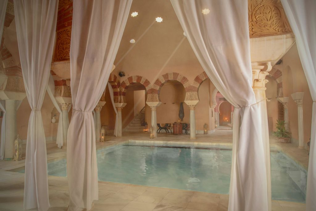실내 수영장은 주변 조명이 있는 따뜻한 분위기의 방에 아치형 기둥과 커튼으로 둘러싸여 있습니다.