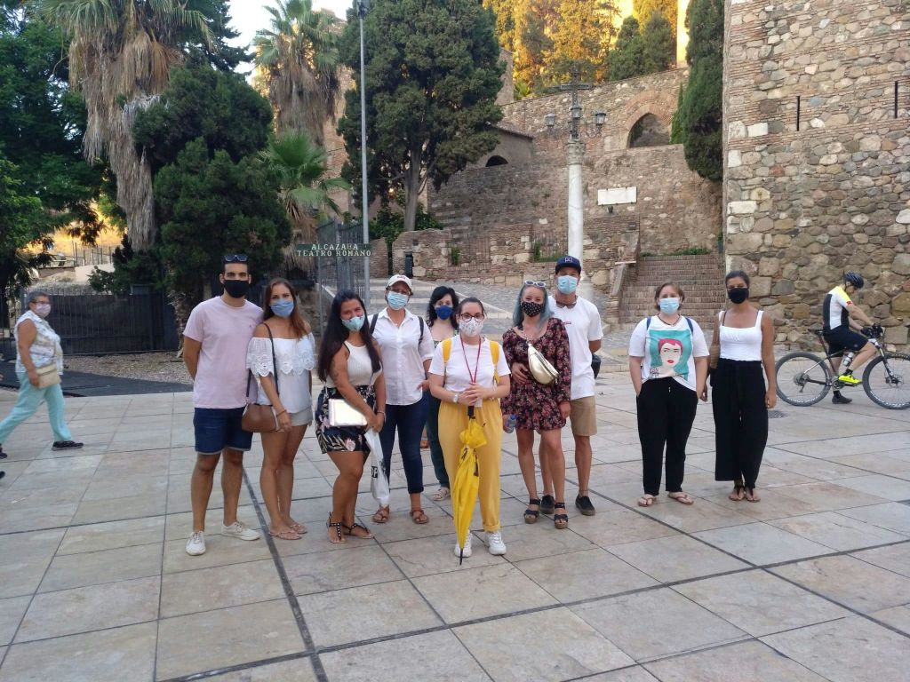 마스크를 착용한 9명의 사람들이 나무와 석조 구조물을 배경으로 야외에서 함께 서 있습니다.