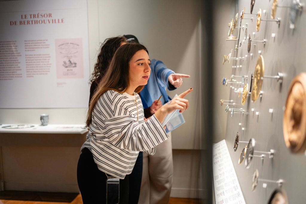 박물관에 있는 두 사람이 작은 물체가 있는 디스플레이를 살펴보고, 한 사람이 물체를 가리키며 흥미롭게 토론하고 있습니다.