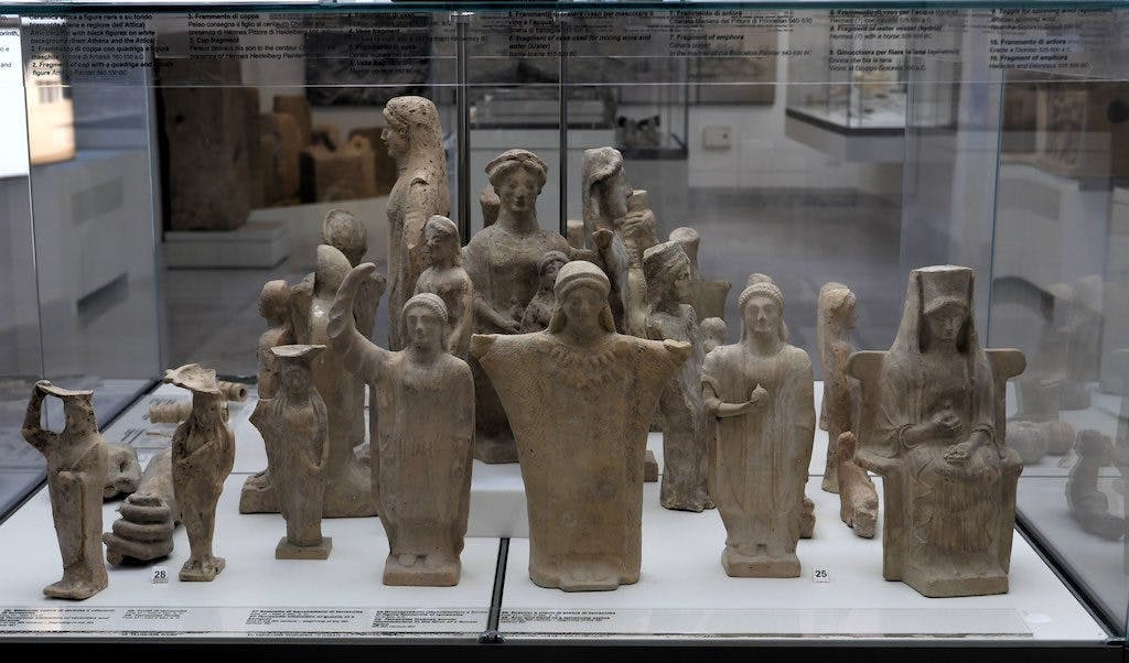 박물관의 유리 상자 뒤에서 다양한 포즈를 취한 사람들의 고대 테라코타 조각상을 전시합니다.